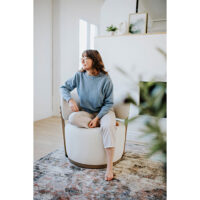 woman relaxing in a custom white swivel chair with exposed wood frame