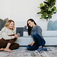 women looking at an ipad on the foor in front of a white channel tufted sofa