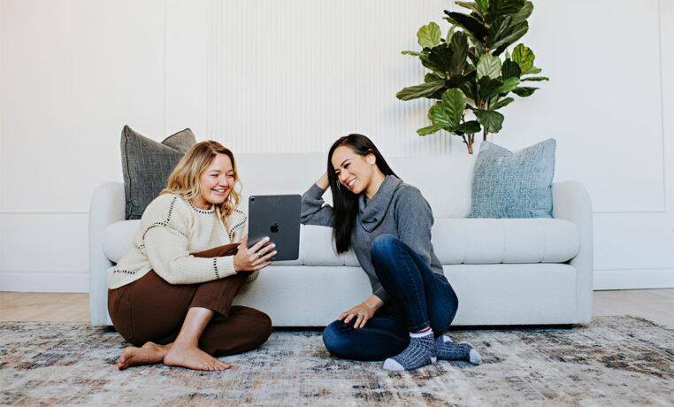 women looking at an ipad on the foor in front of a white channel tufted sofa