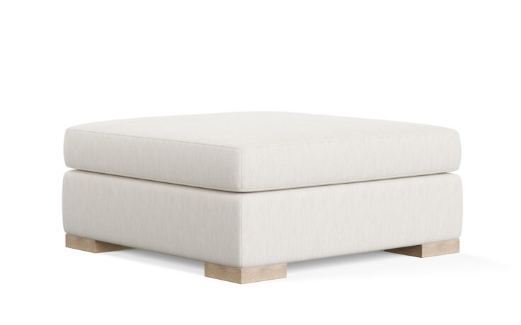Angled shot of the oversized, plush Broadway ottoman from Vogel by Chervin in a white fabric with light wood legs